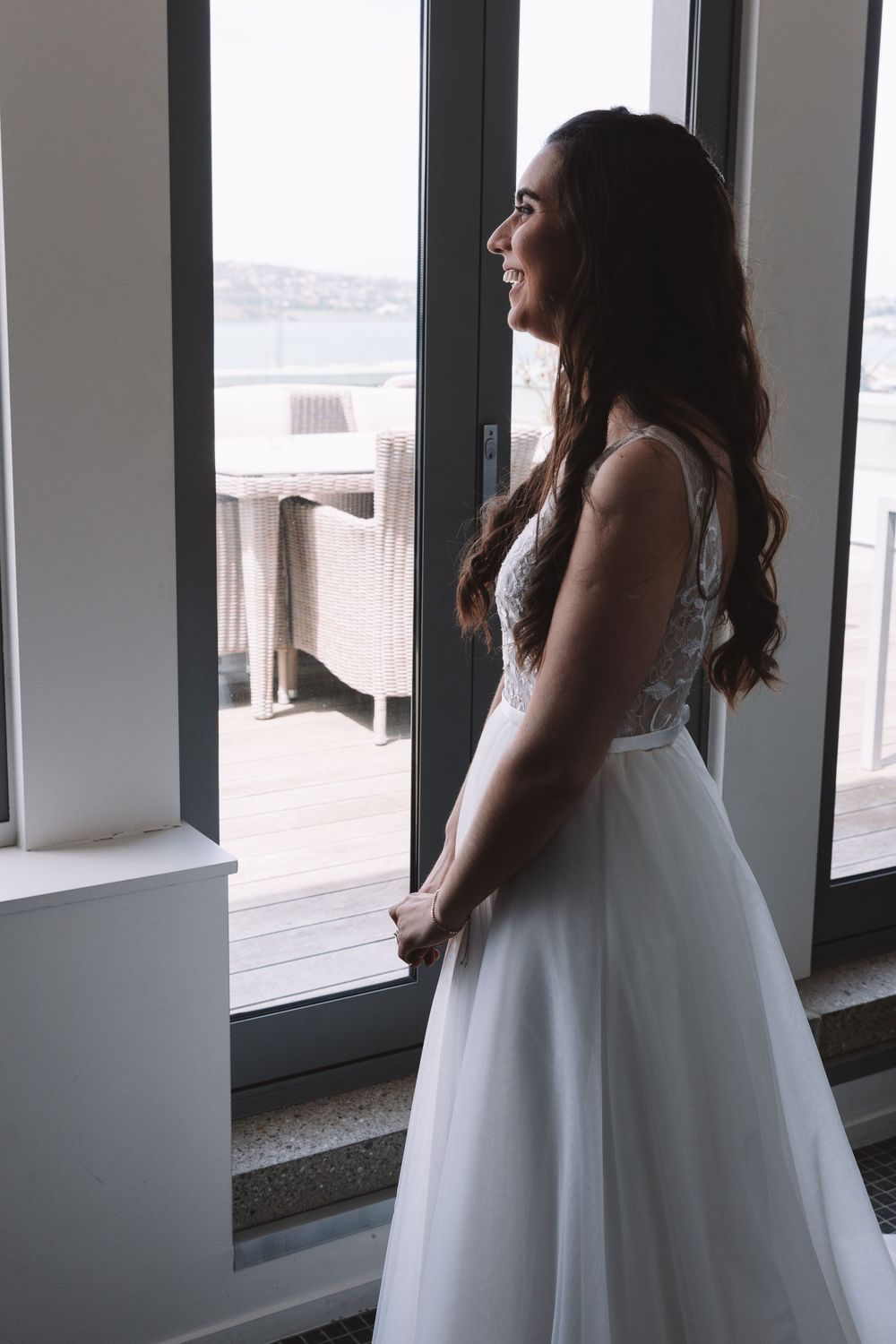 A bride in a lace and tulle wedding gown gazes out a large window.