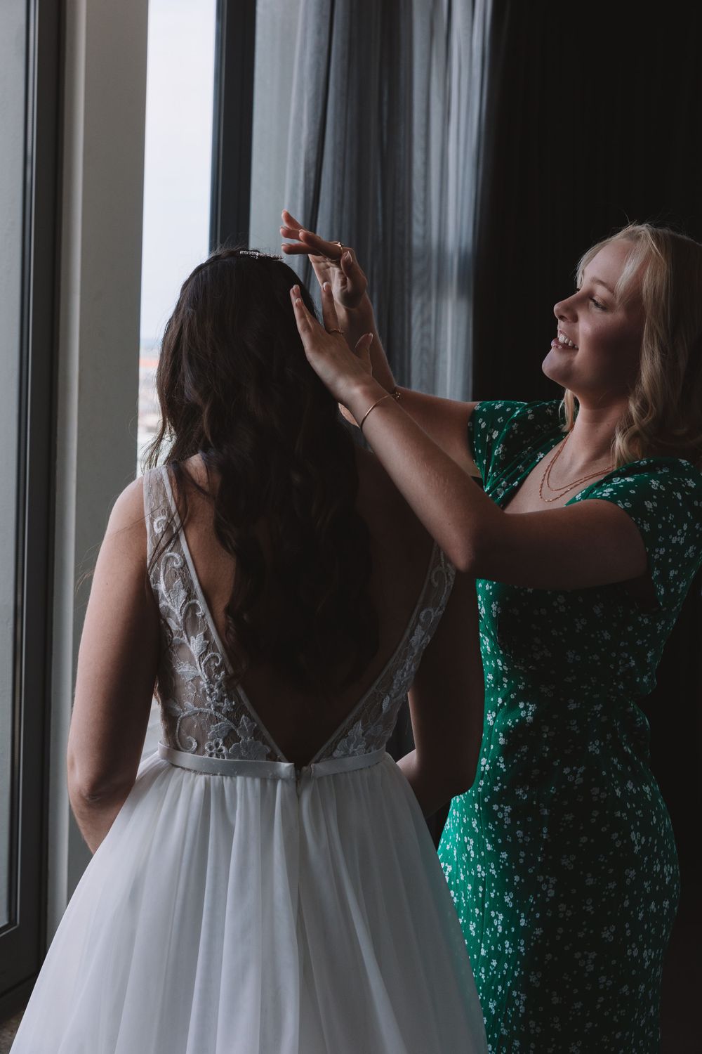 A woman in a green sequin dress helps adjust the bride's wedding gown.