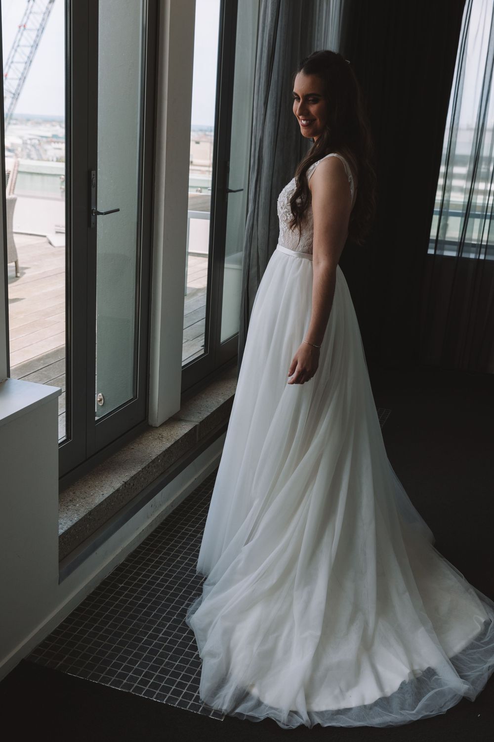A bride poses in her white lace wedding gown with a flowing train against window light.