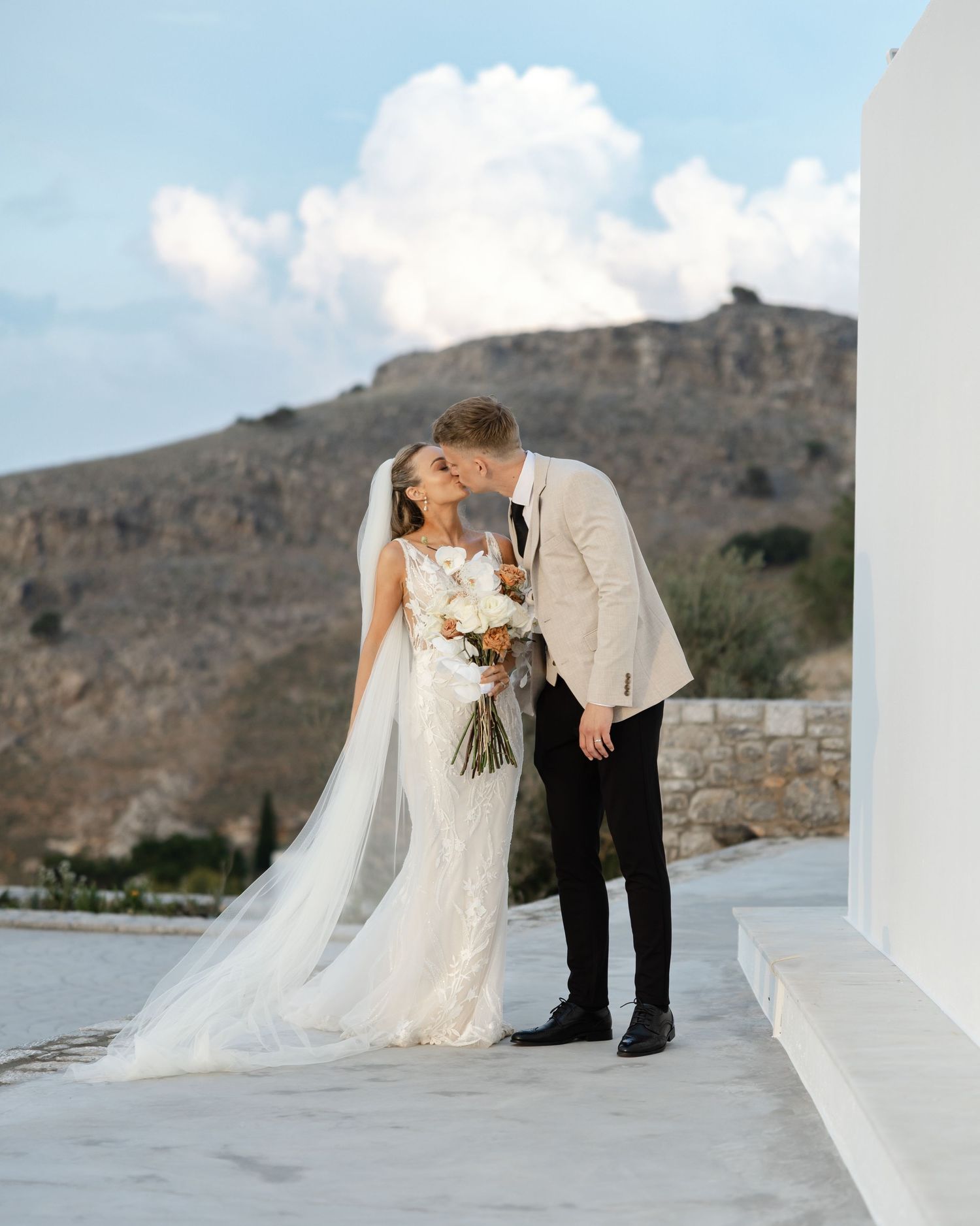 A couple sharing an intimate moment on a rooftop terrace with dramatic cliffs and blue sky in the background.