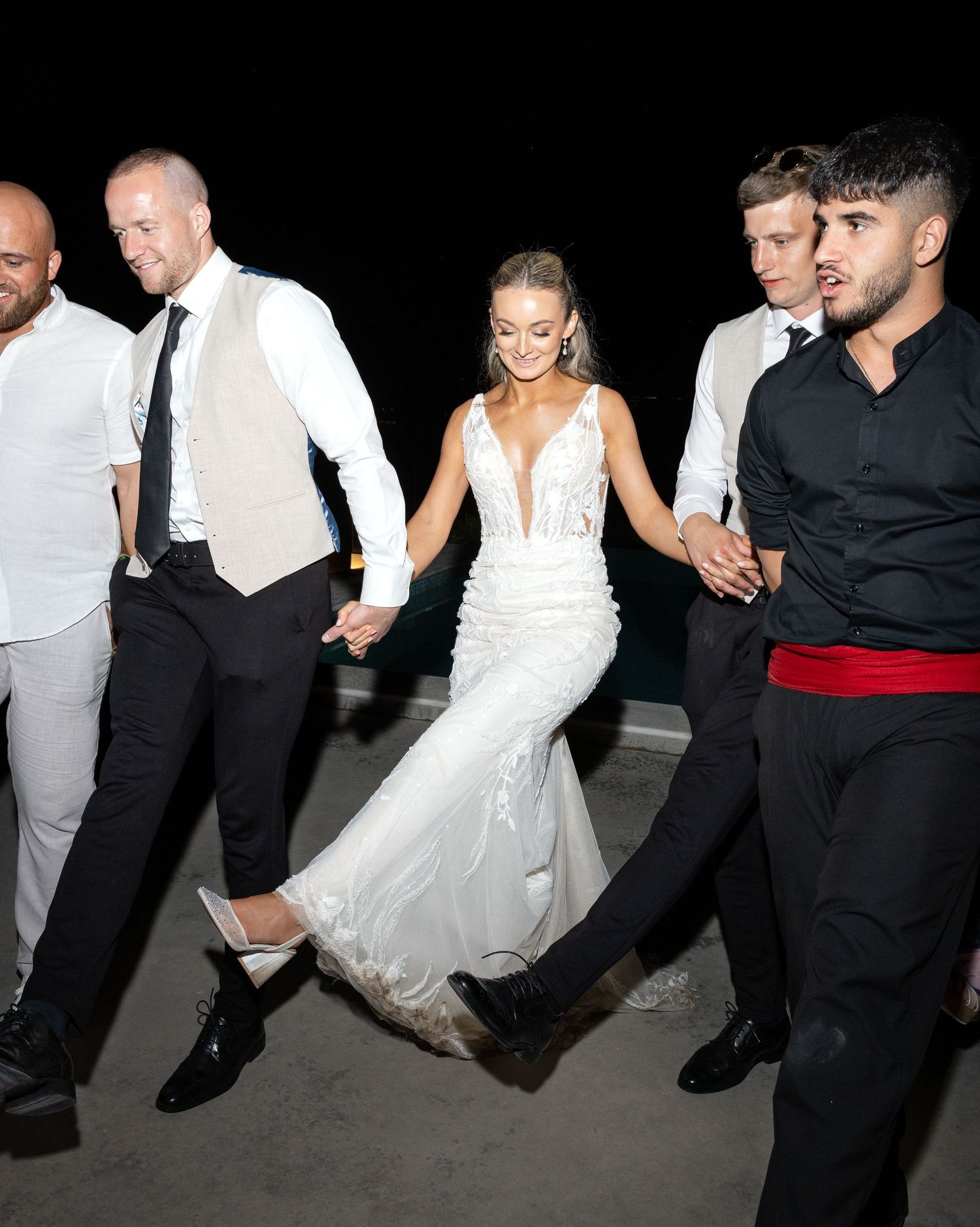 Wedding party dancing together in celebration, with the bride in a white gown and others dressed in formal attire.