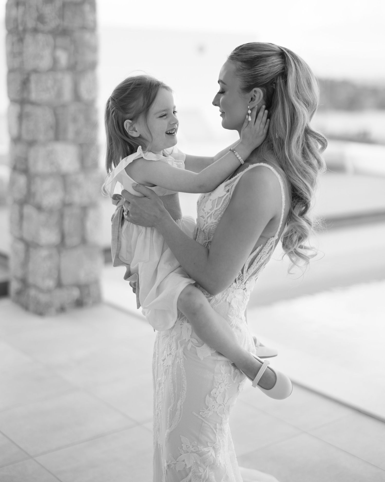 A tender black and white portrait shows a heartwarming embrace between a woman in a lace dress and a child.