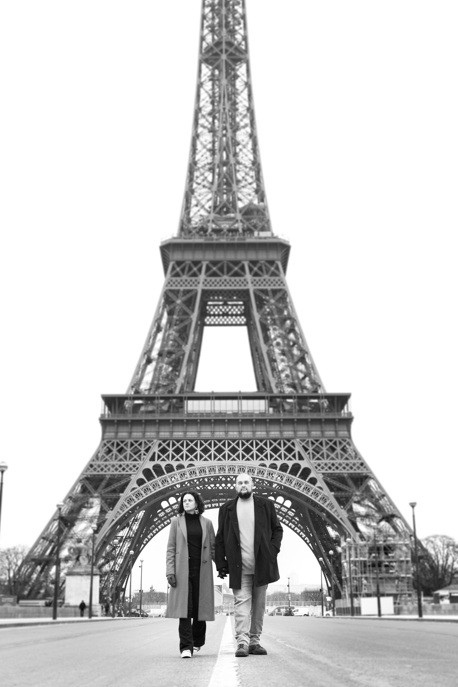 A black and white photograph of two people standing beneath the Eiffel Tower.