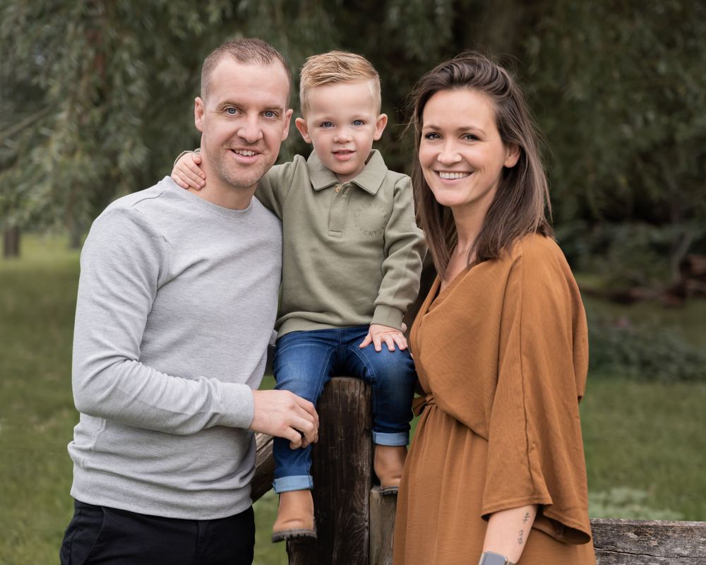 liefdevolle familie foto van ouders met een zoontje in het midden, zoontje zit op een hek en ze kijken in de camera. zachte en warme kleuren