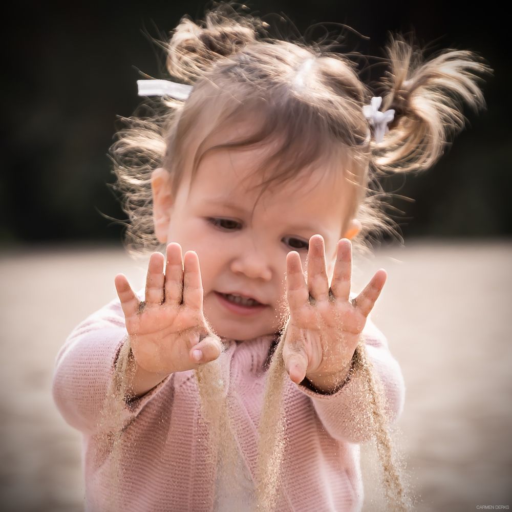 foto van meisje op een strand, meisje laat zand door haar handen gaan en kijkt ernaar. gefotografeerd in maas en waal op een buitenlocatie.
