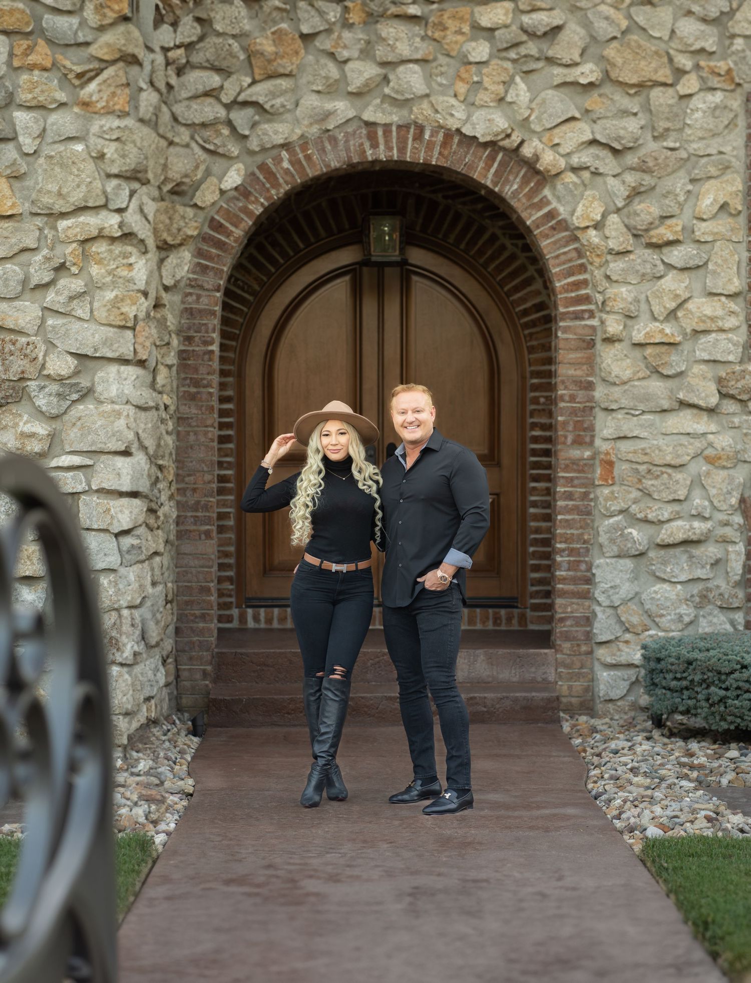 Couple posing under a stone archway entrance with brick and stone walls.