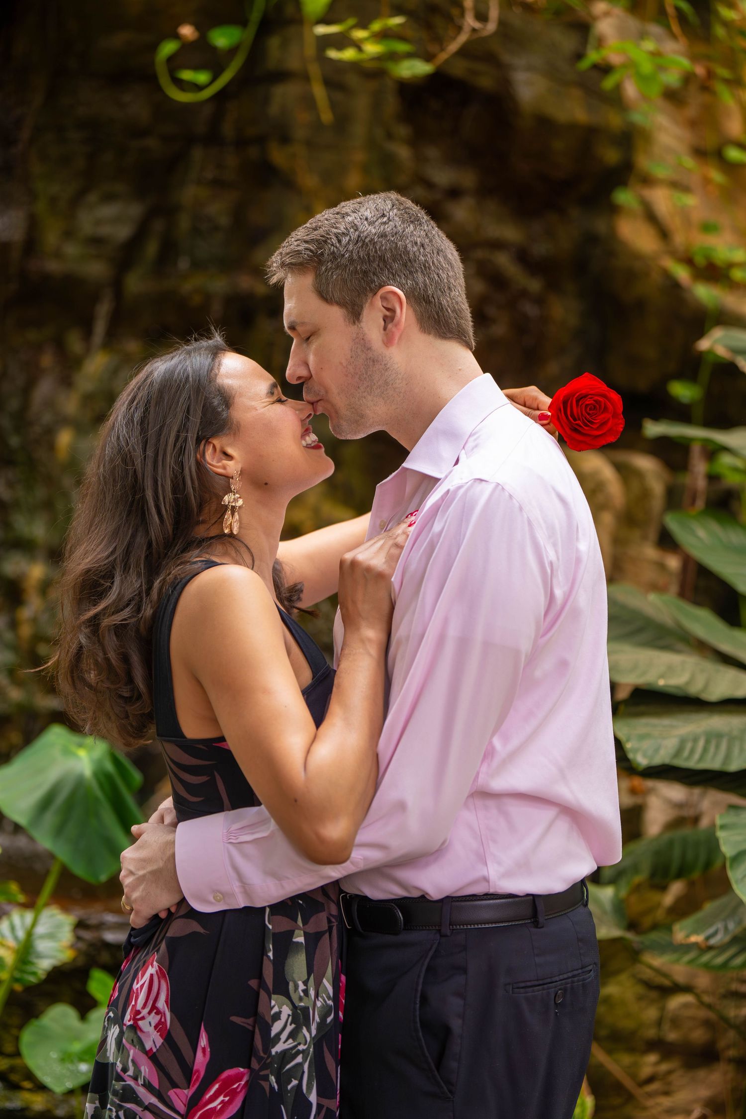 Romantic couple embracing in a lush garden setting with red flowers.