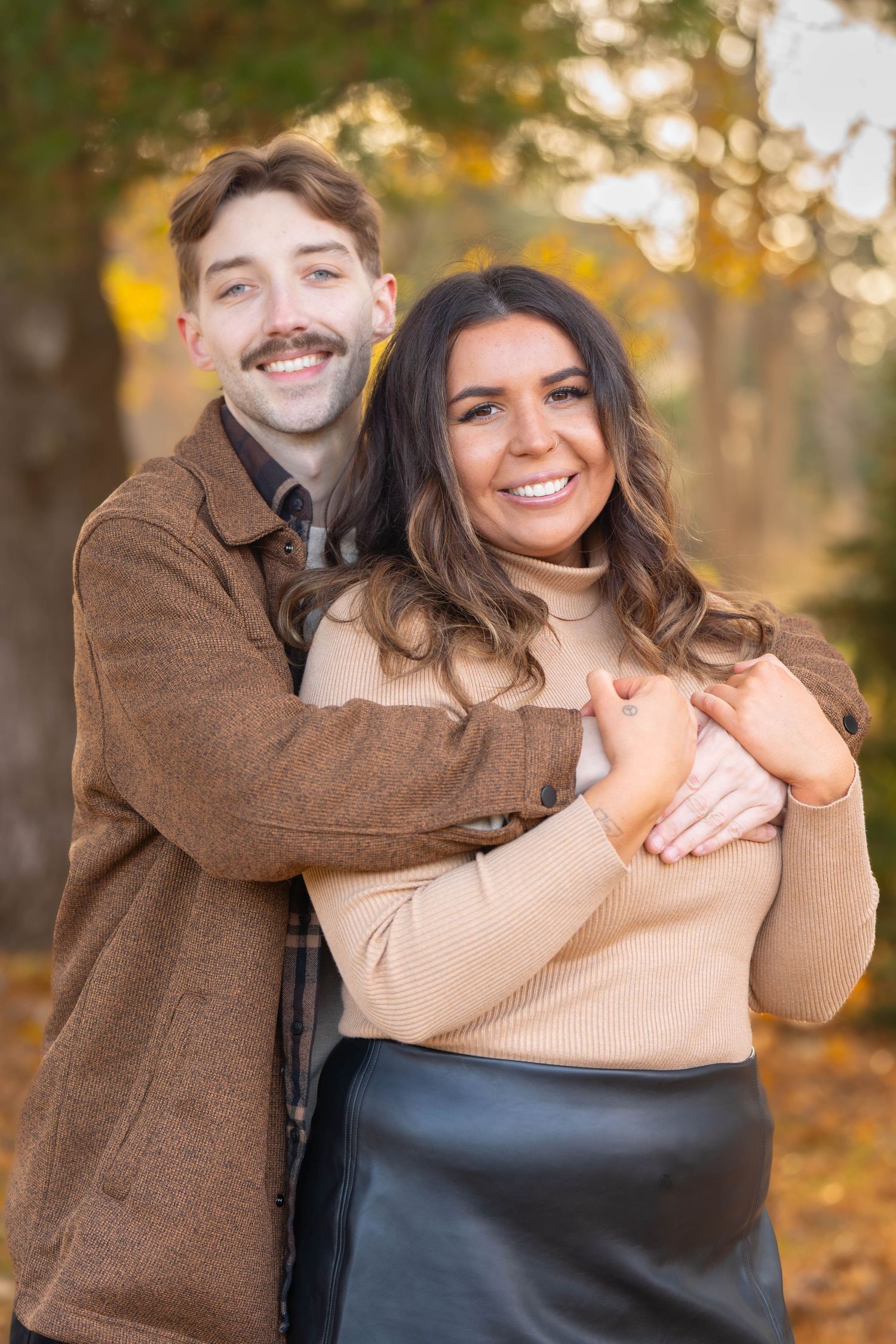Autumn portrait of a couple embracing outdoors with fall foliage in background.