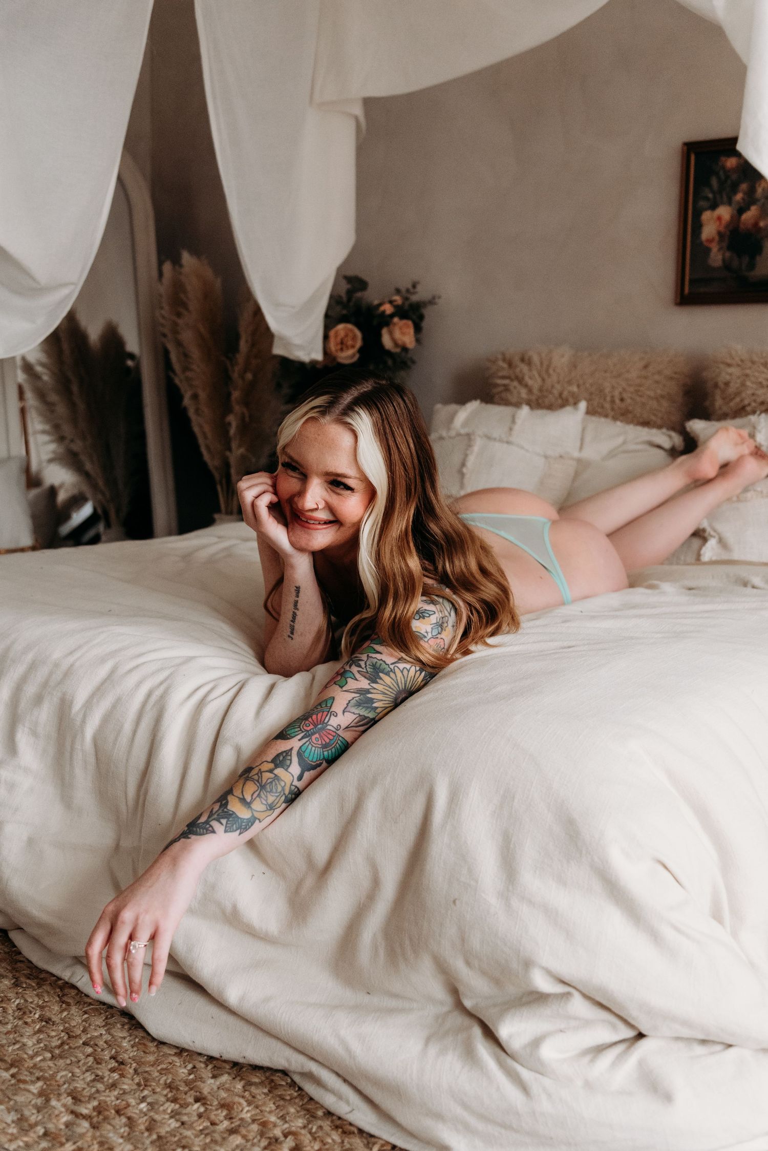 A person lying on a white bed decorated with pampas grass and floral artwork in a cozy bedroom setting.
