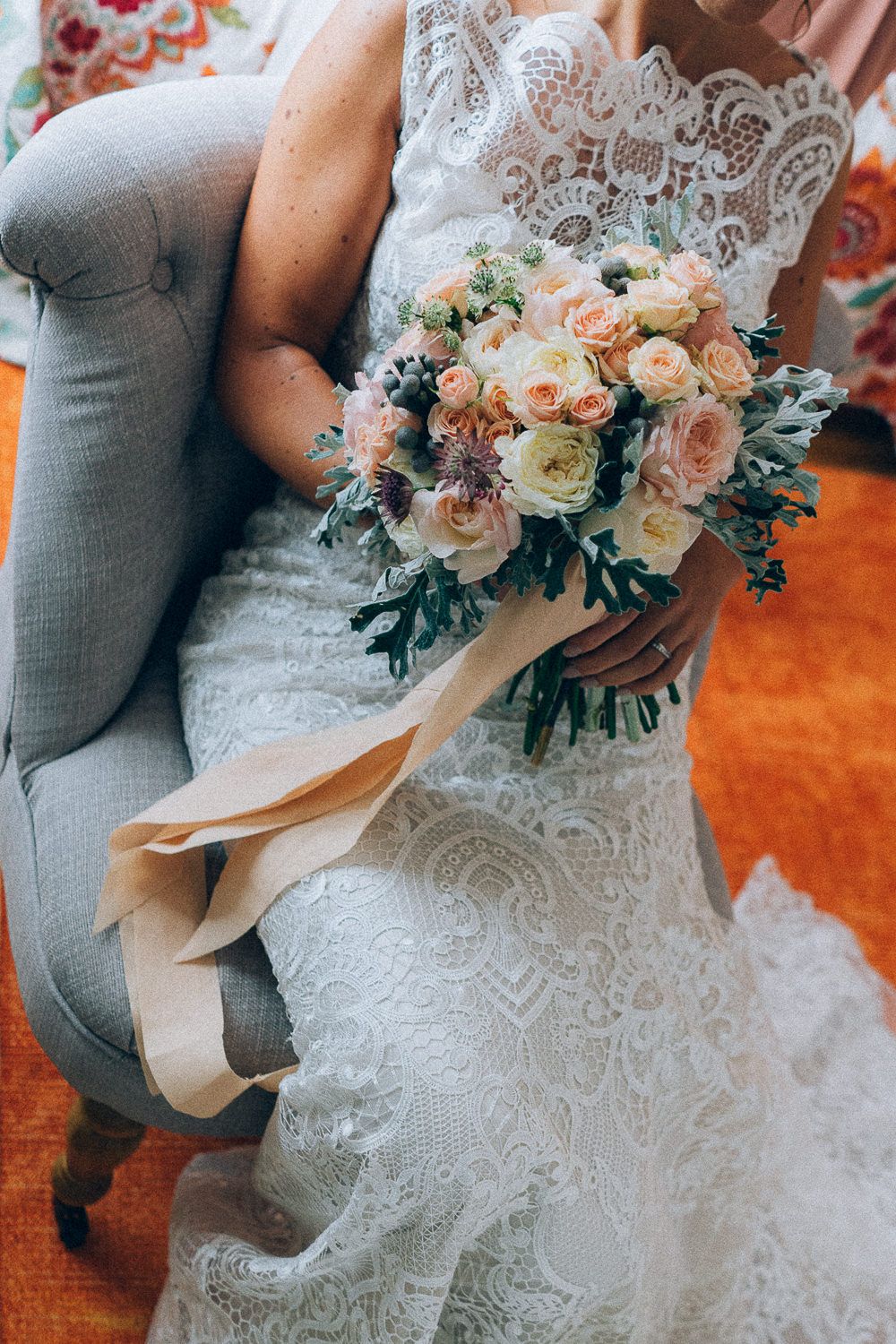 noiva numa cadeira a segurar o boquet, flores rosa e brancas, com fita rosa
