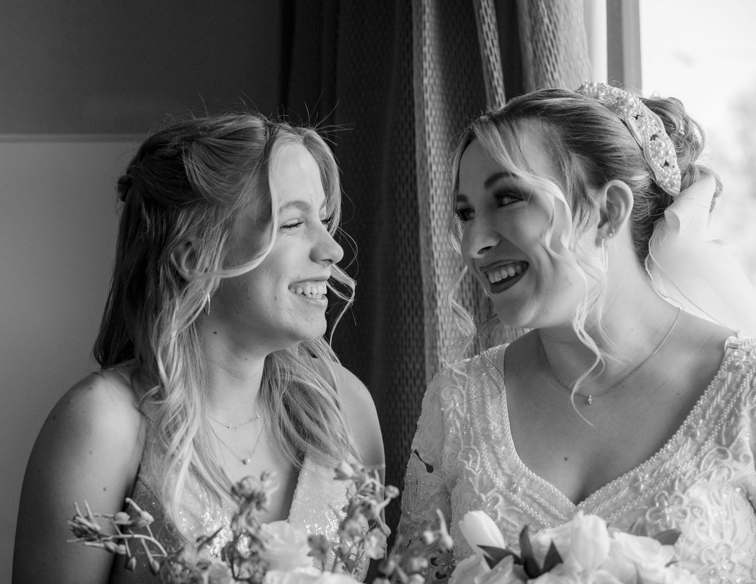 Black and white portrait of two wedding attendants sharing a joyful laugh.