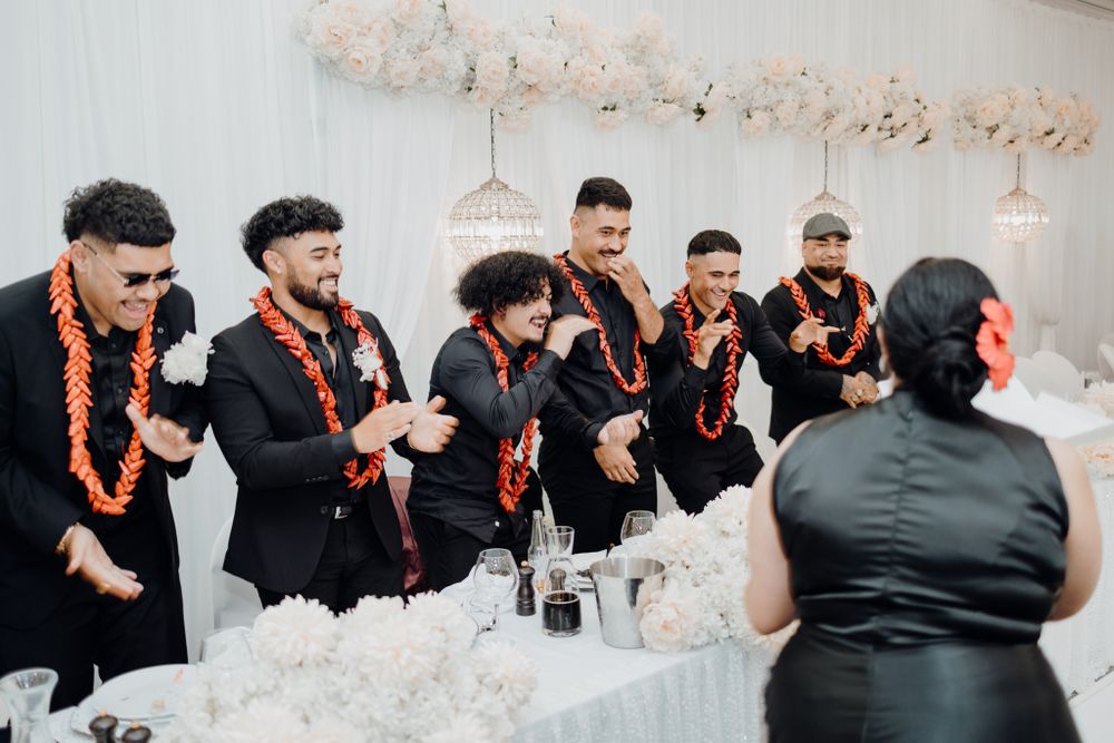 Group in black formal wear with orange leis celebrate at wedding reception.
