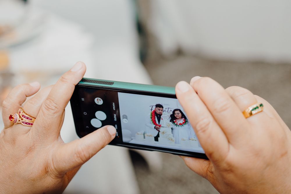 Hands holding phone to capture wedding moments with gold rings visible.