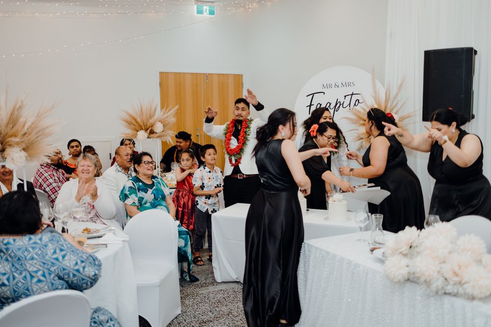 Wedding reception guests dance and celebrate under decorative lighting and pampas grass decor.