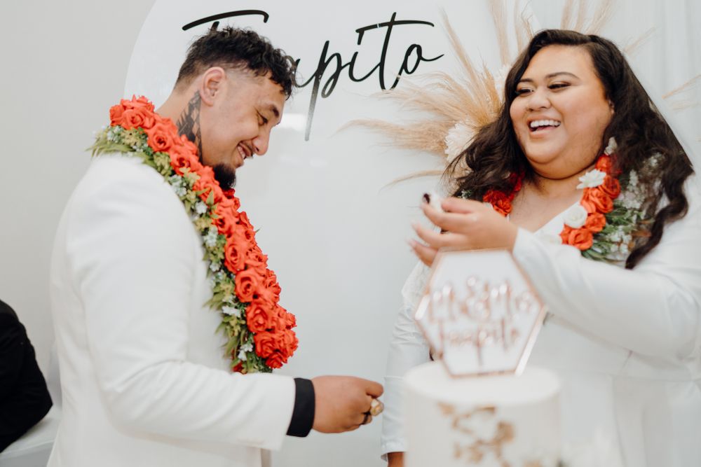 Newlyweds share joyful moment while wearing traditional orange flower leis.