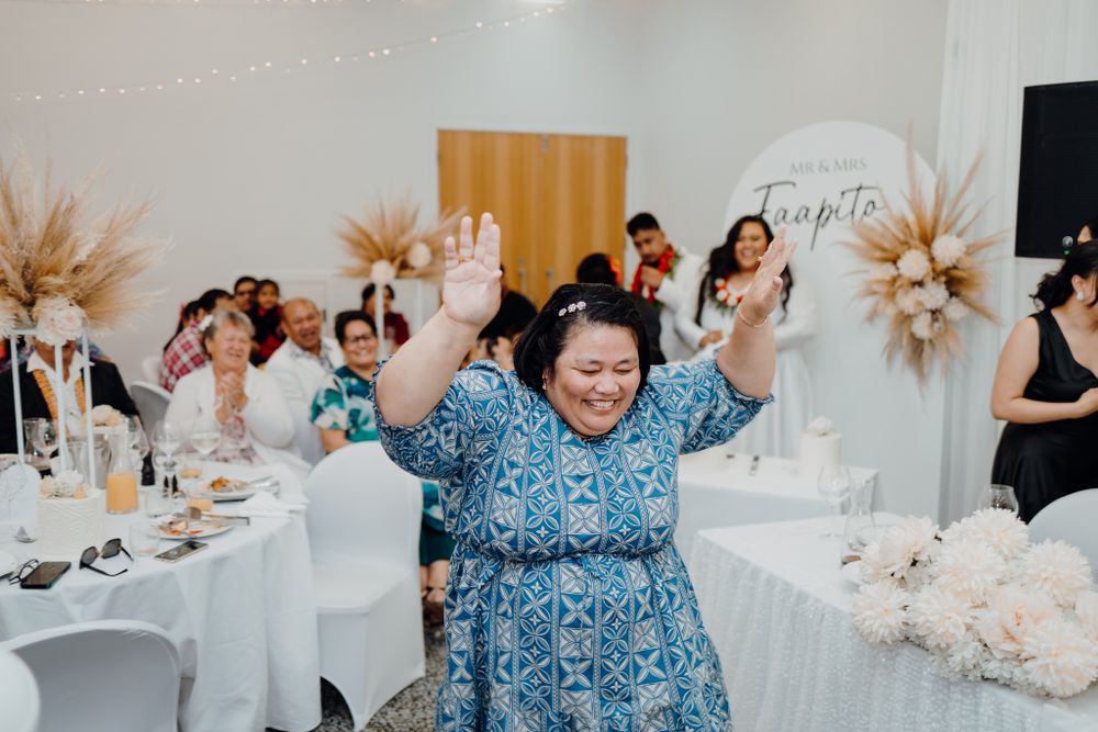 Guest in blue patterned dress dances enthusiastically at wedding reception.