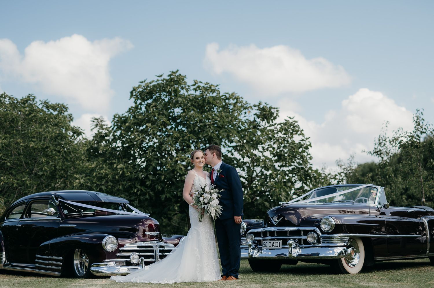 wedding couple pose in front of vintage cars