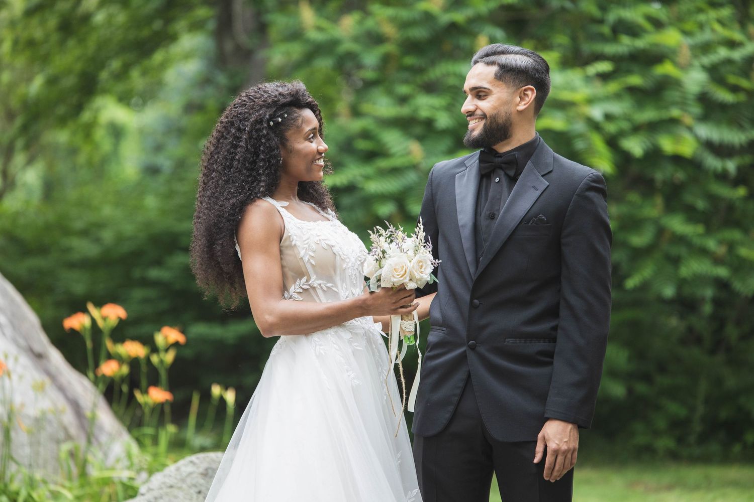 A joyful wedding couple shares a candid moment in a garden setting with lush greenery and yellow flowers.