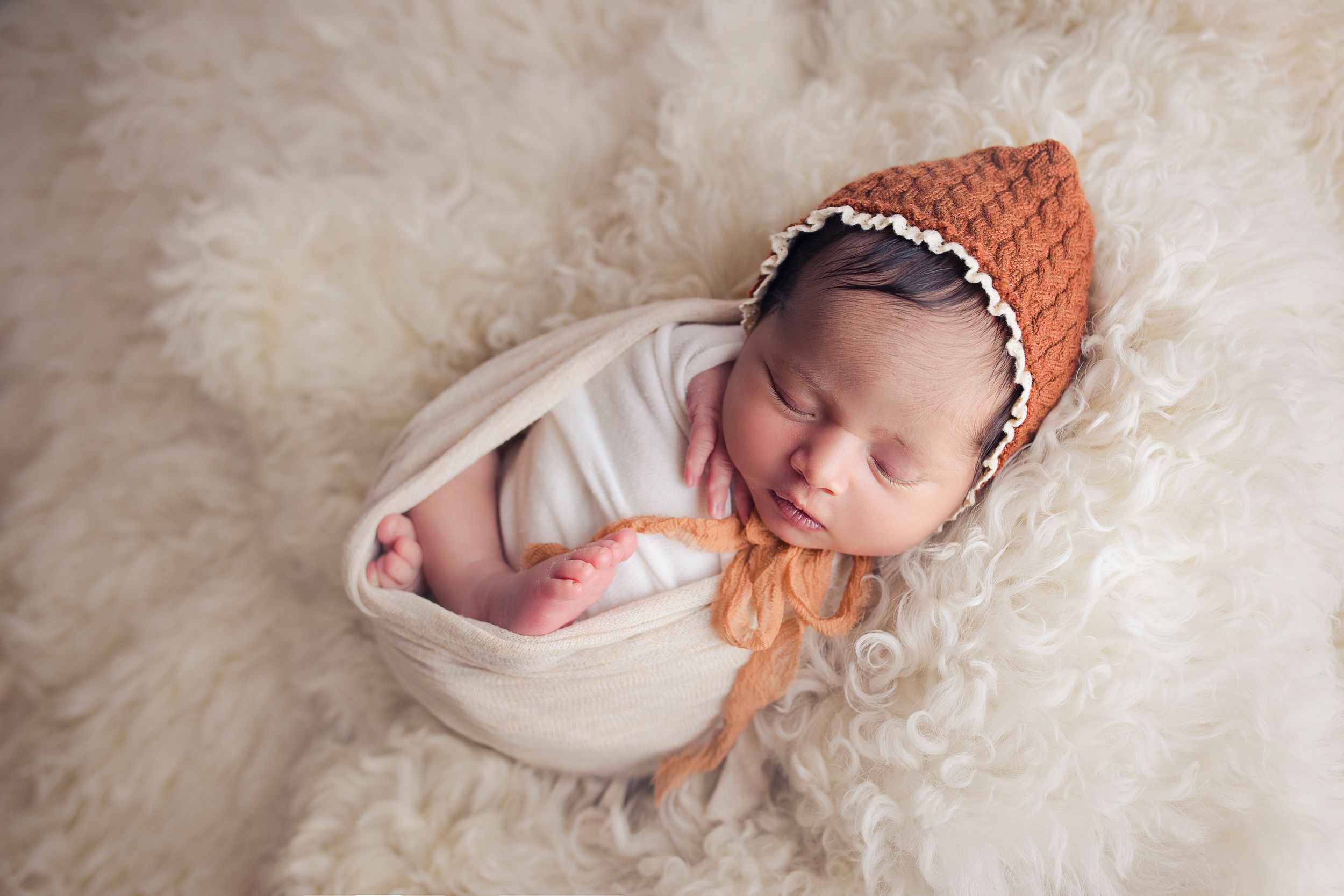 newborn baby girl with terracotta bonnet wrapped in white