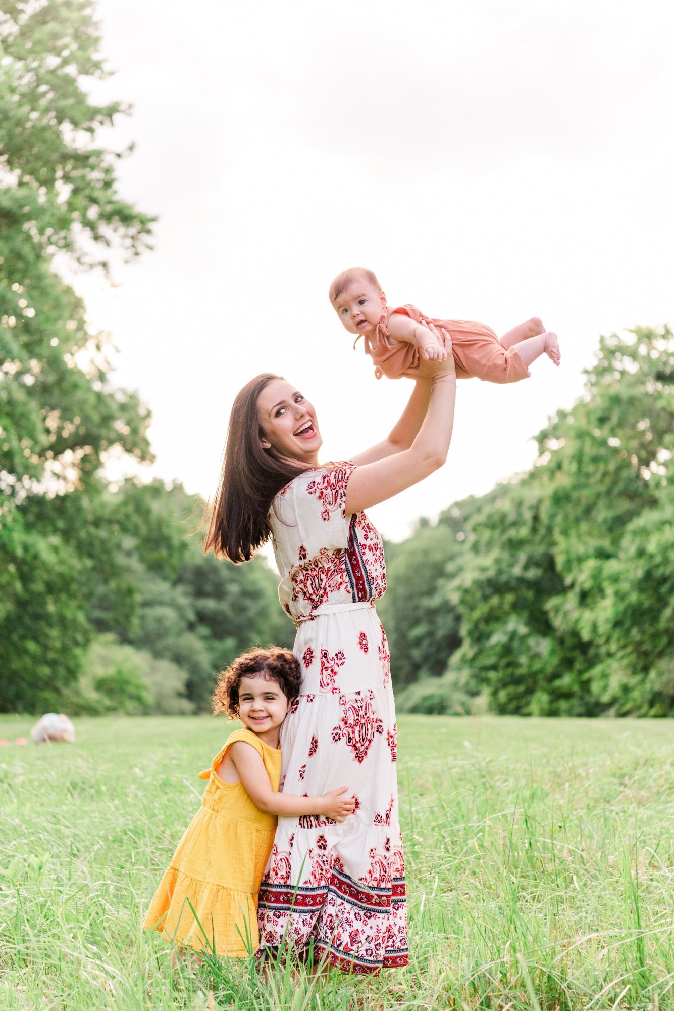 Mother holding baby up in the air while young daughter hugs her legs in Pittsburgh, Pennsylvania