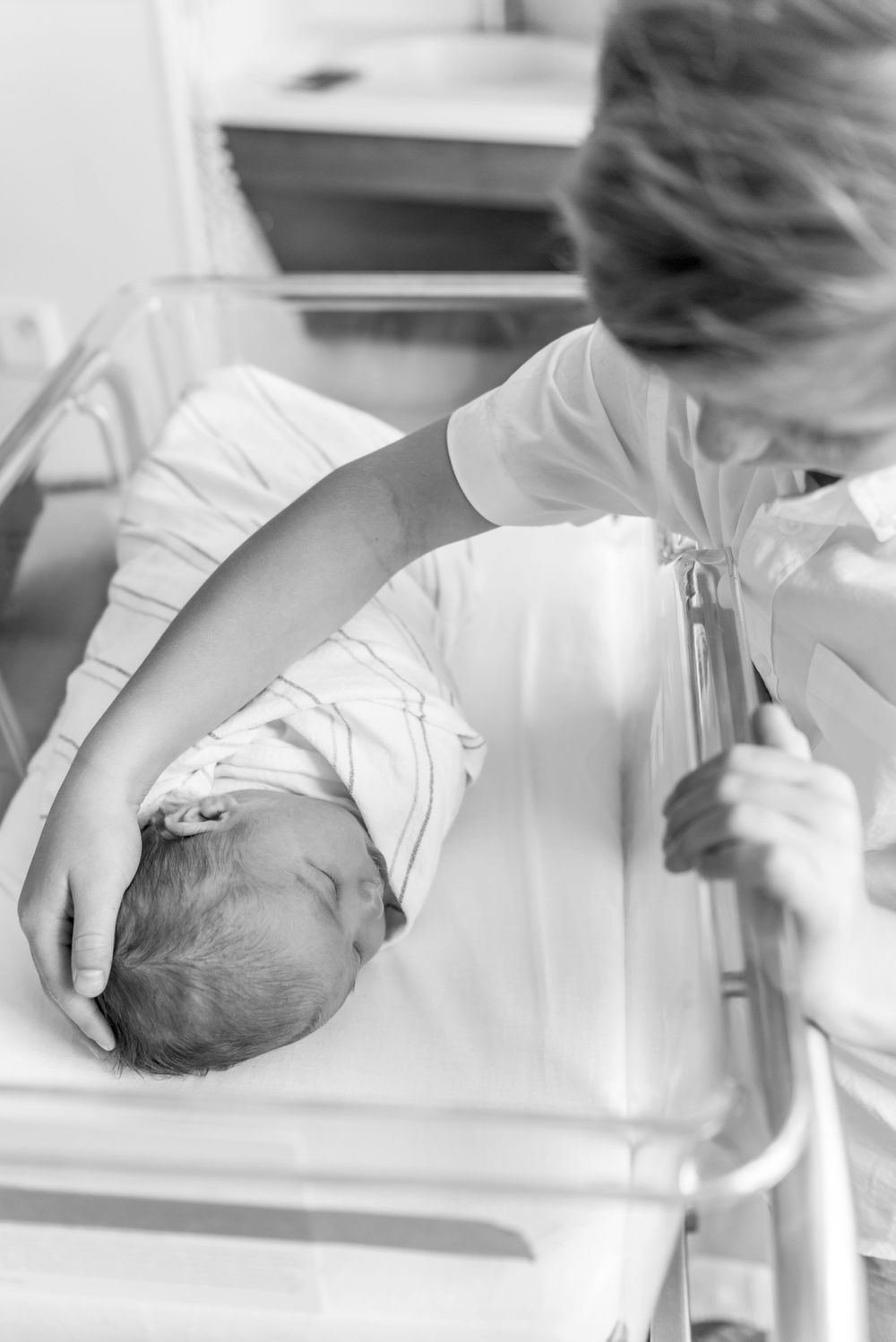 Big brother leaning over bassinet, cradling new baby's head. Fresh 48 Session by Heidi Harting Photography