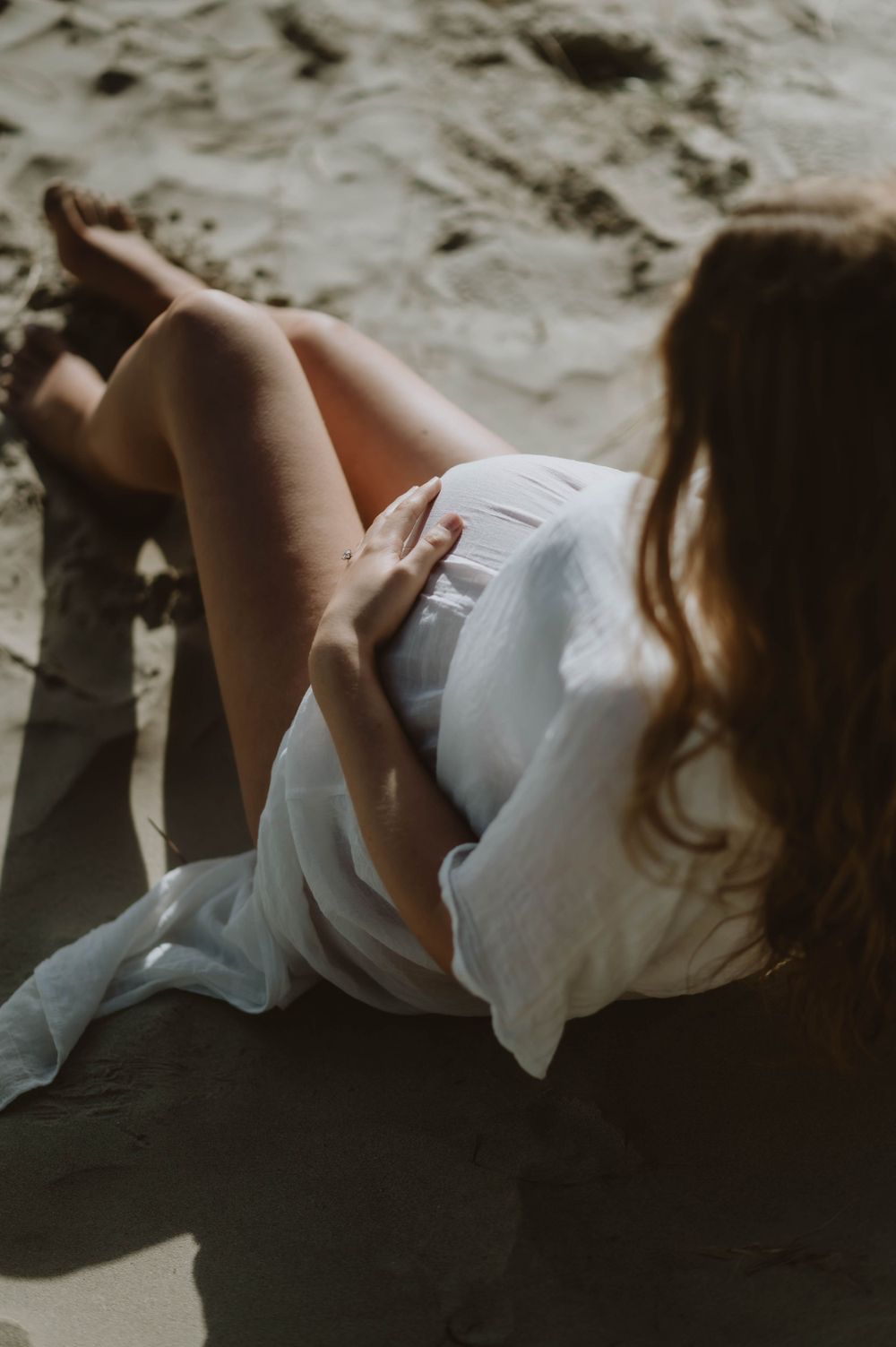 Artistic beach maternity photo with soft lighting and flowing white fabric.