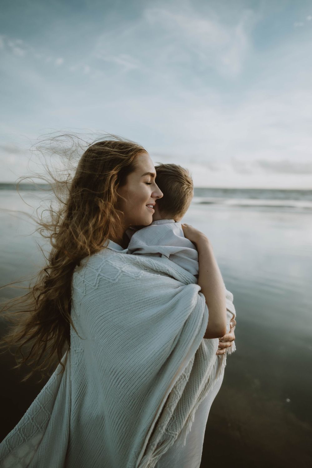 A touching moment by the ocean as wind blows through hair on a misty beach at dusk.