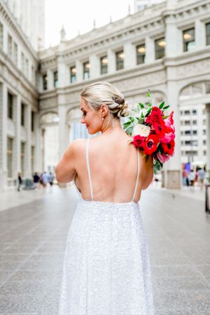 blonde woman in silver sequin dress holding red bouquet under Wrigley Building after downtown Chicago elopement