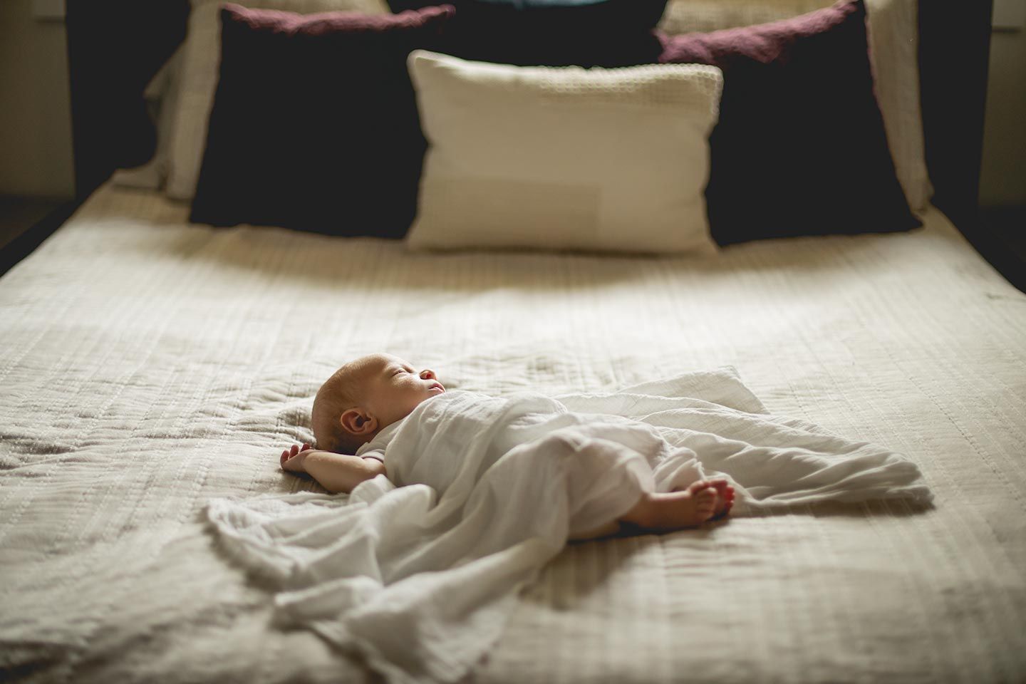 newborn baby sleeping on bed with light blanket covering him