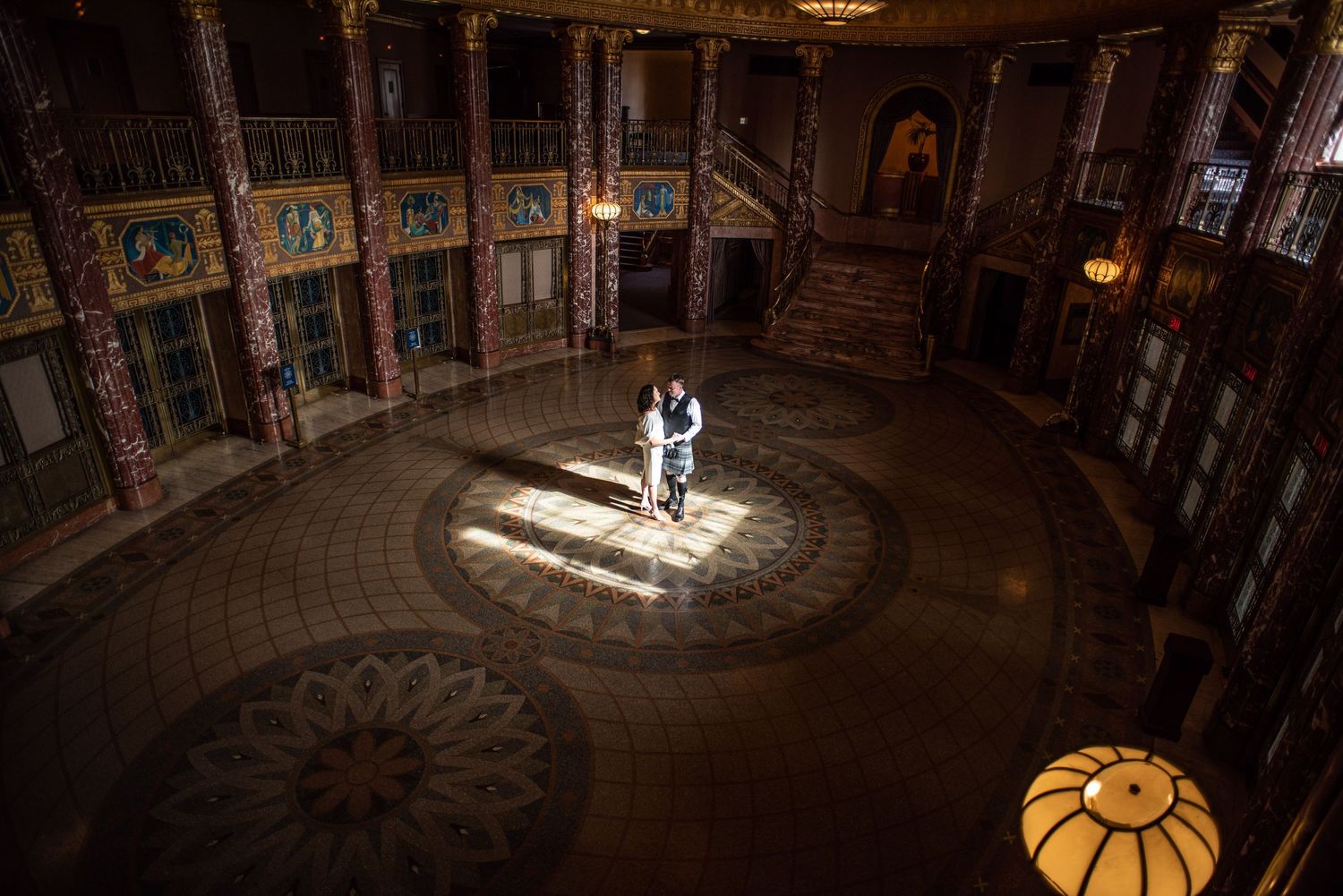 couple stands in the middle of Severance Hall lobby illuminated by sunlight