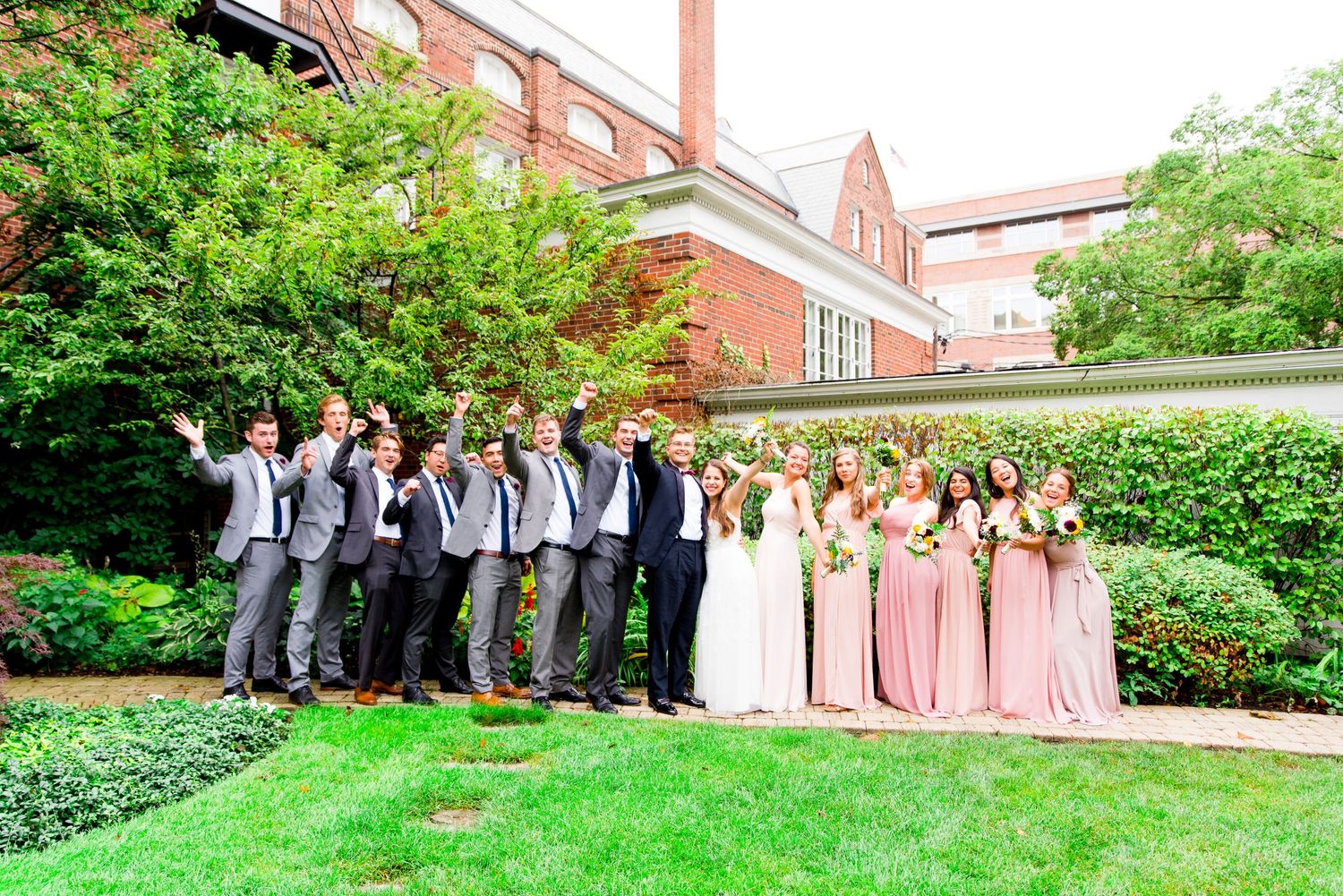 wedding party in grey suits and pink dresses cheer for bride and groom in Woman's Club of Evanston garden