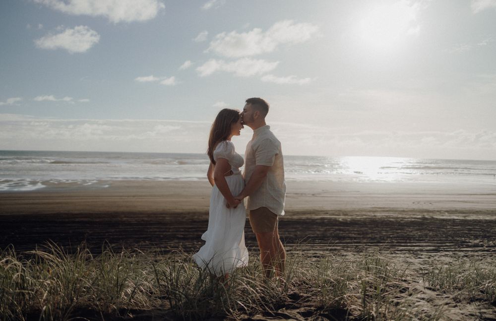 Couple embracing on a beach at sunset with ocean waves in the background.