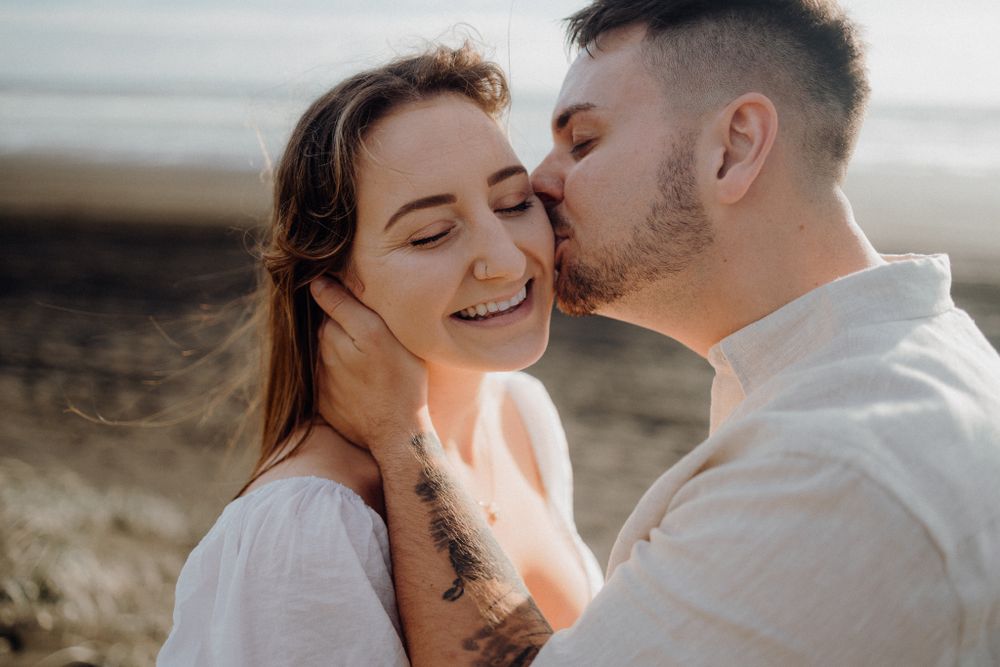 Intimate moment shared between couple against natural coastal background.