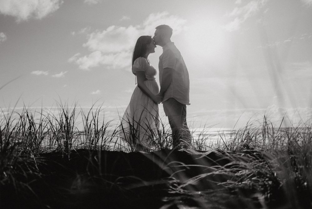 Silhouetted couple embracing on sand dunes against cloudy sky in black and white.