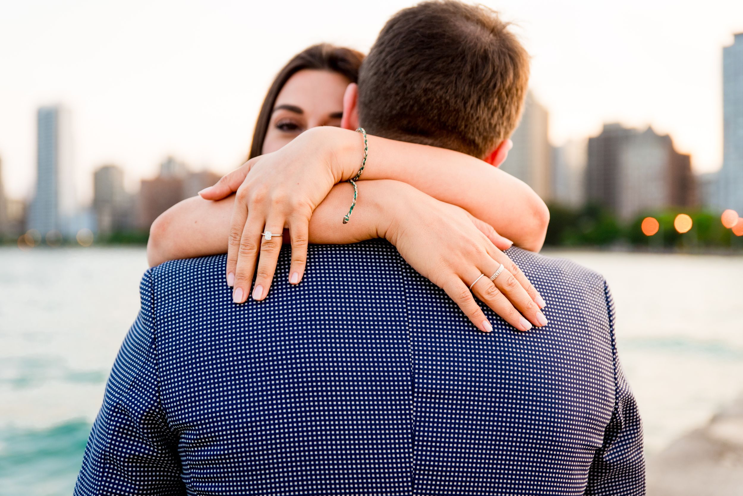 woman hugging new fiance showing off her ring and peeking over his shoulder