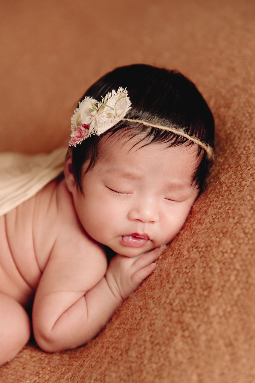 close up of baby girl sleeping on tummy on brown blanket back rolls visable