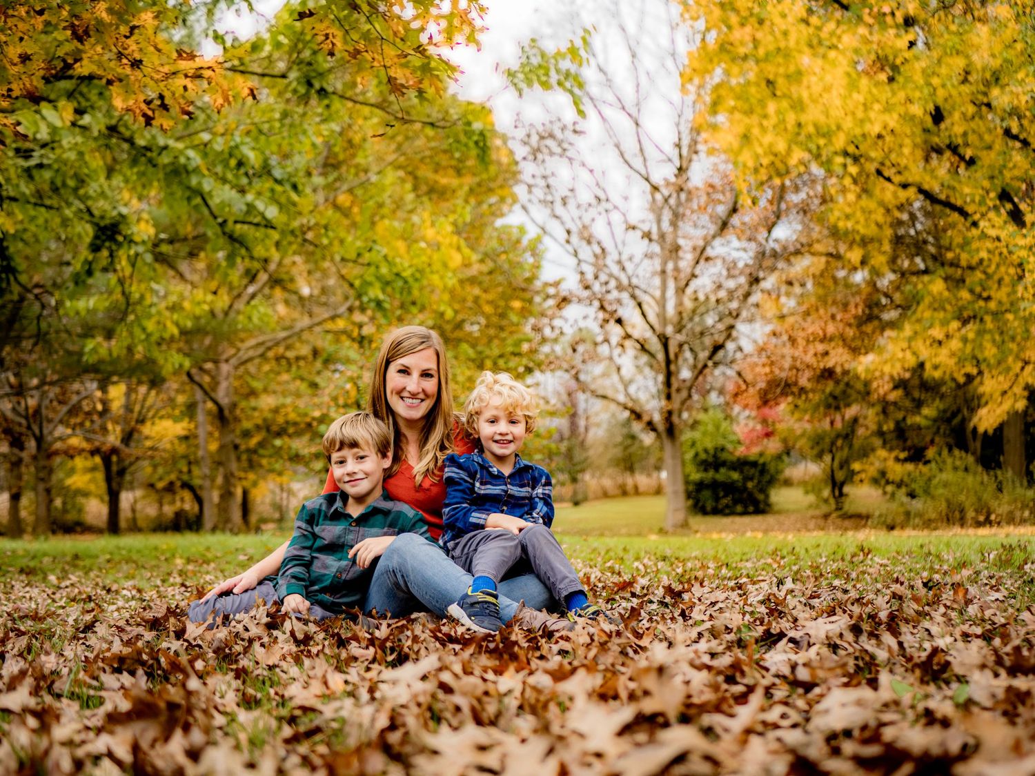 People sitting together on fallen autumn leaves in a park.