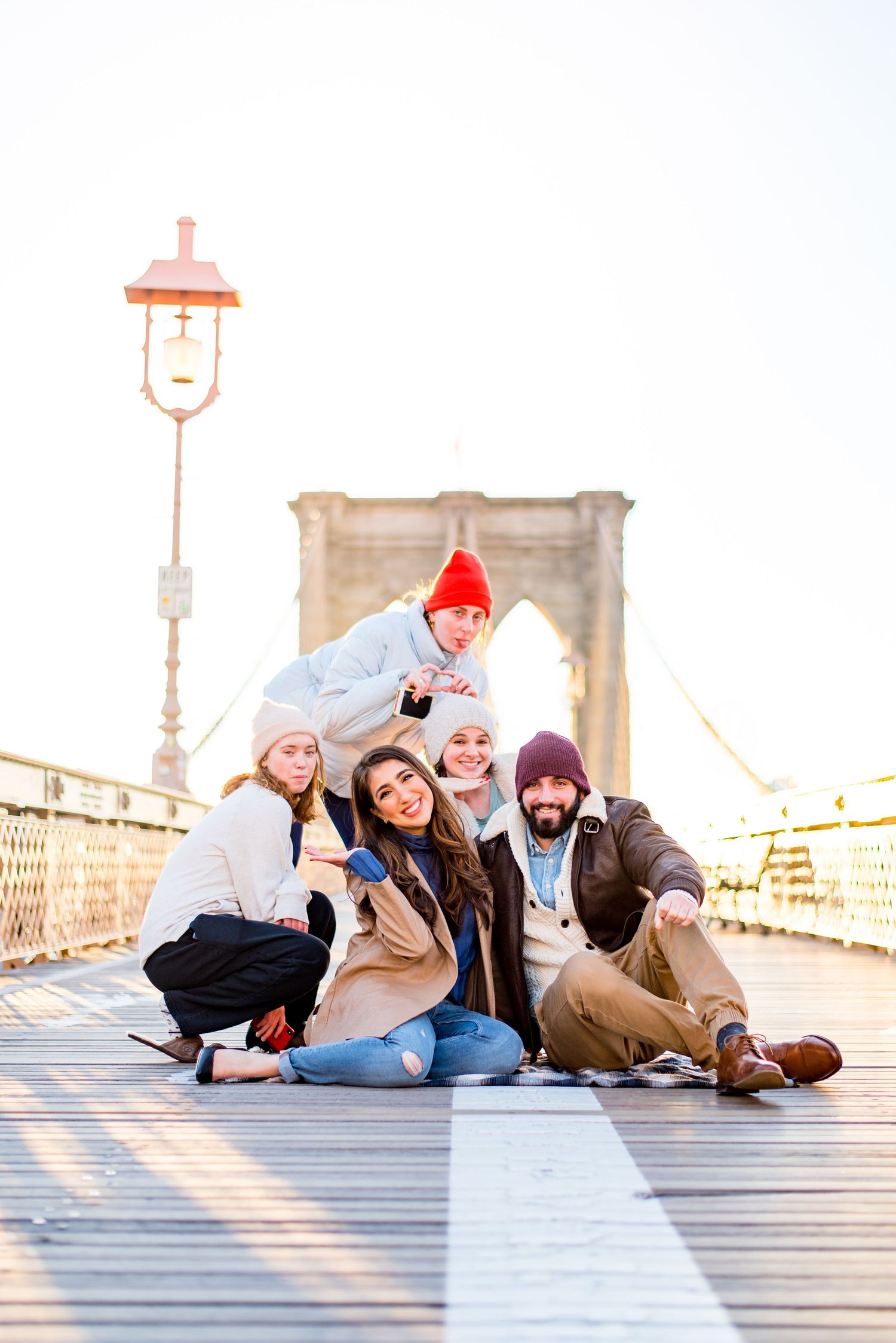 three strangers in NYC smile with an engaged couple in the middle of Brooklyn Bridge at sunrise