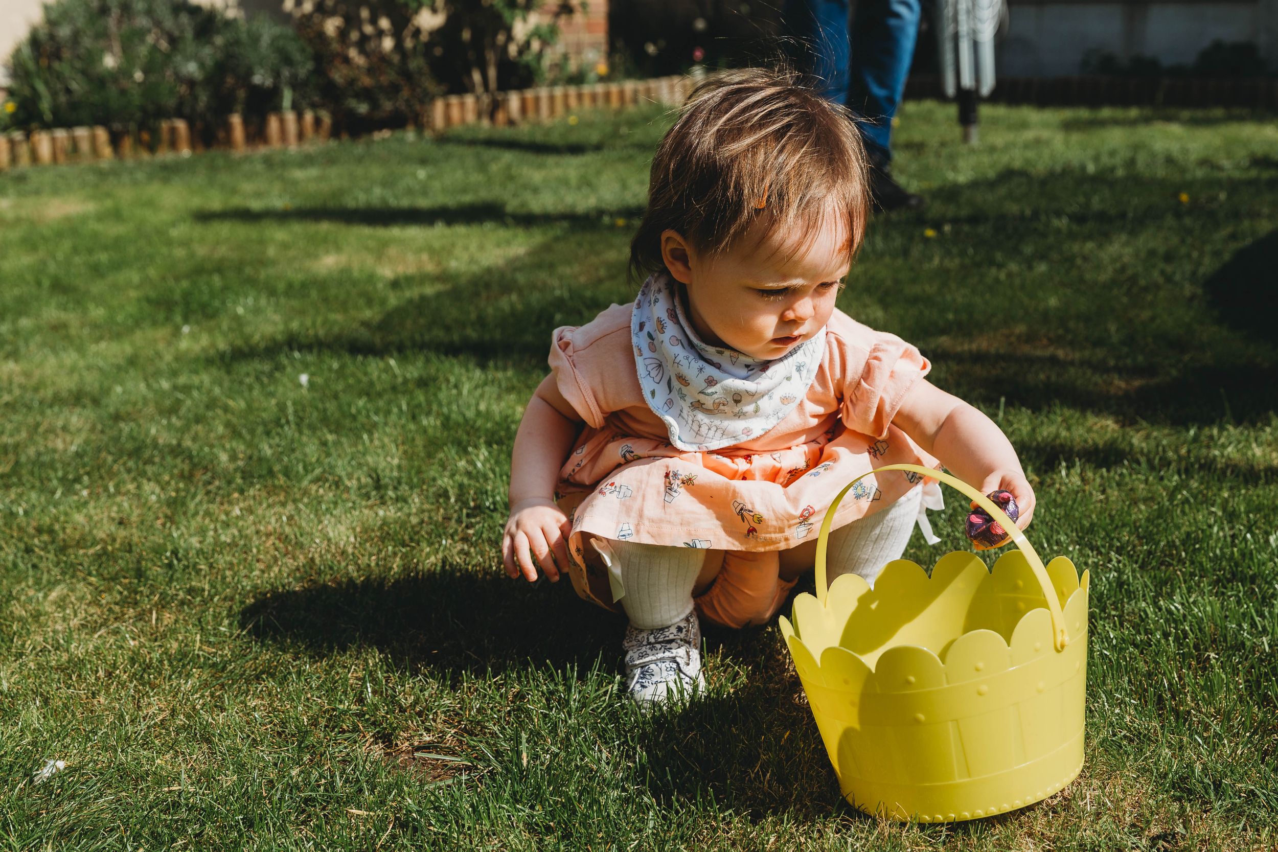 little girl in peach dress with yellow bucket looking for chocolate eggs