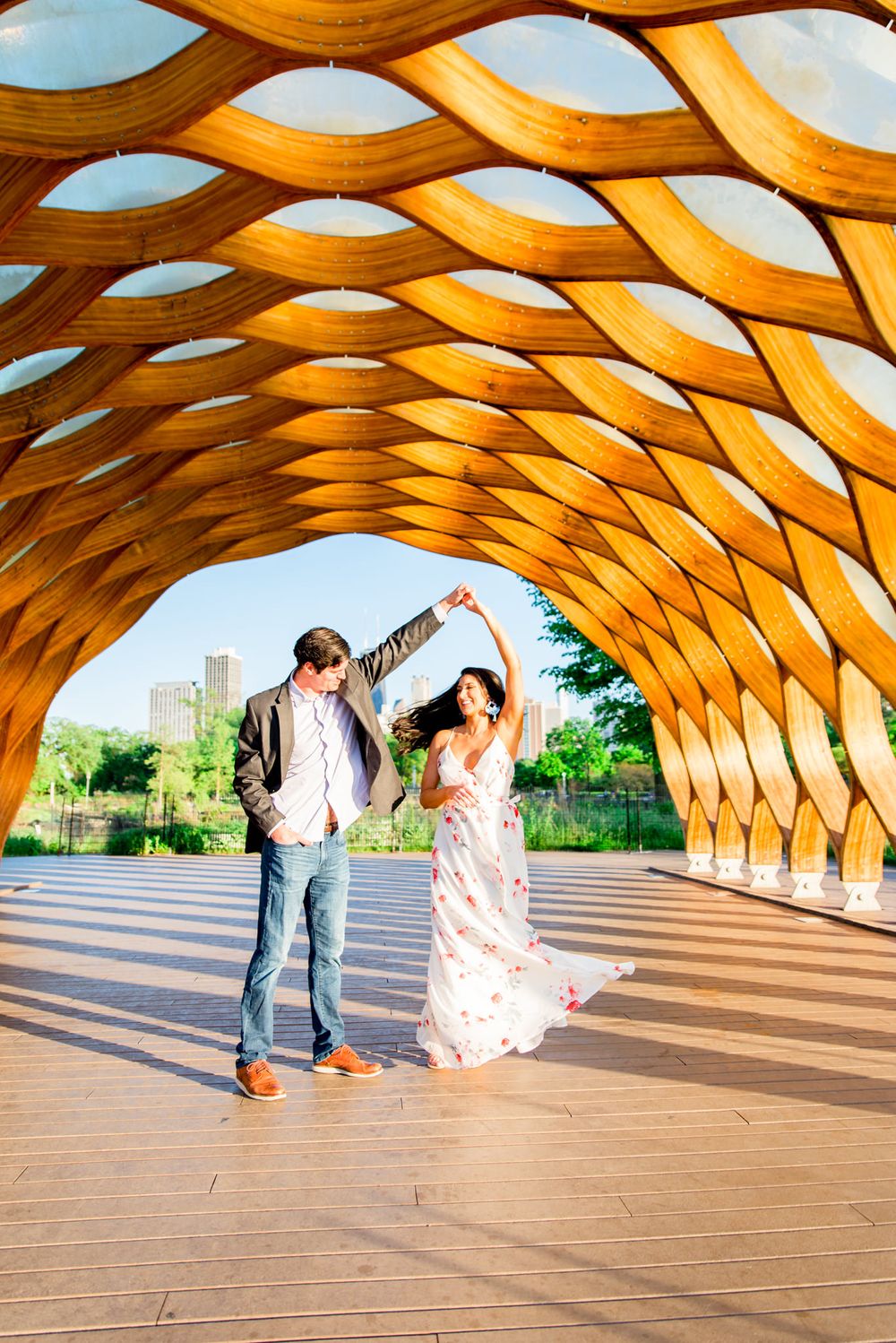 man in suit twirling woman under Honeycomb at Lincoln Park for engagement pictures in Chicago at sunset