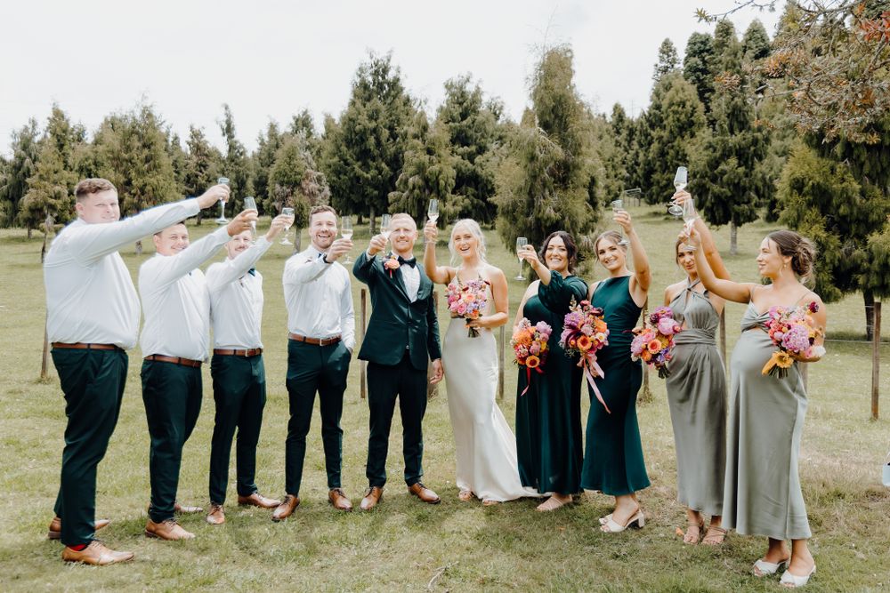 Wedding party poses together with raised arms celebrating outdoors.
