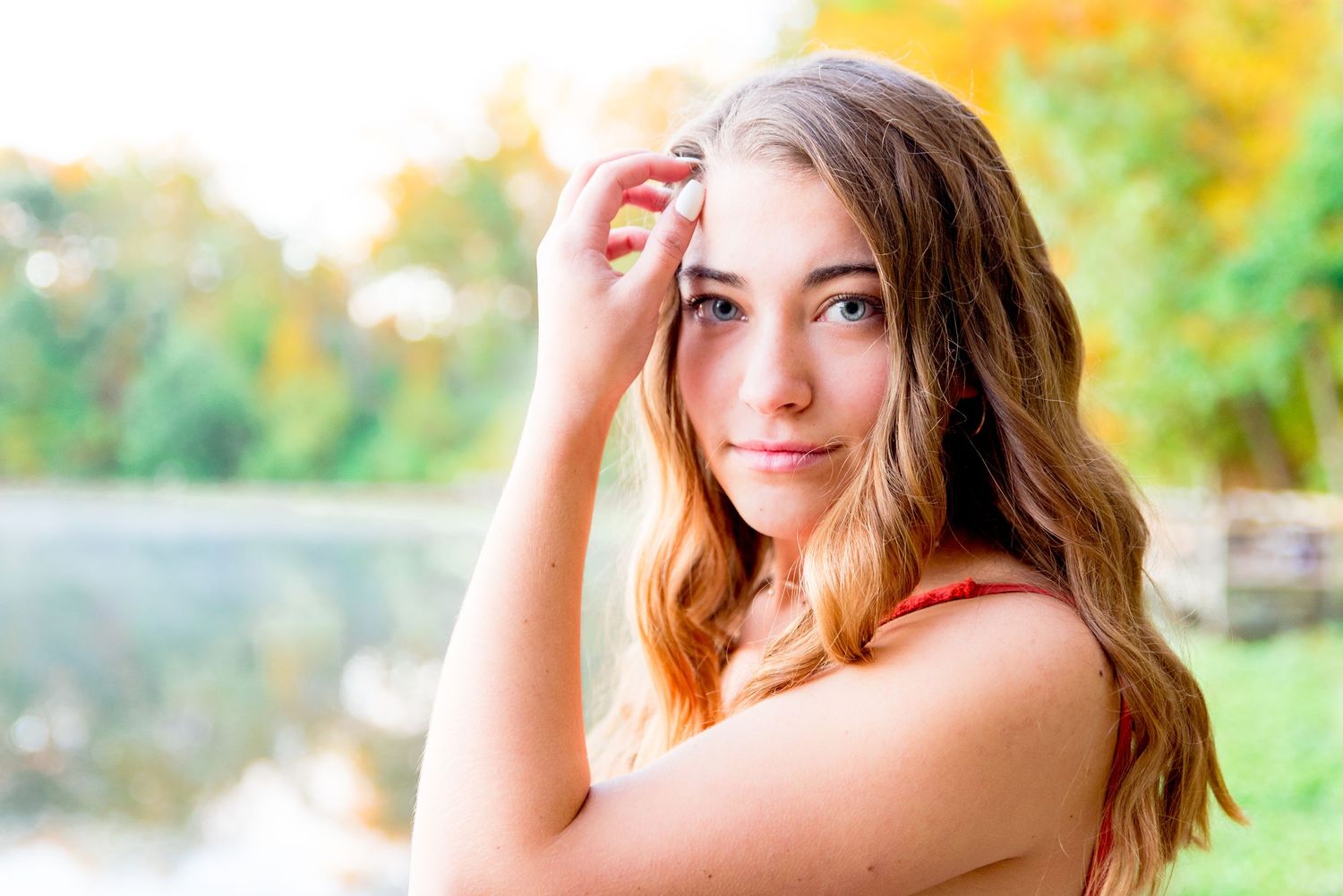 young woman with blue eyes in an orange jumpsuit stands in front of foggy lake with fall foliage in Chicago