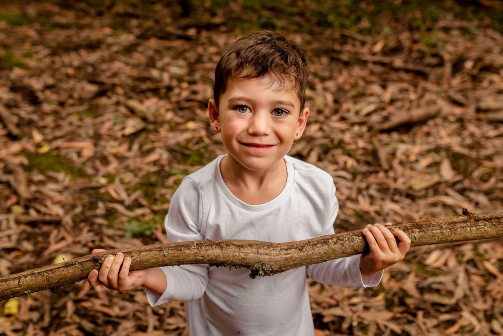 Boy in white tshirt holding branch in forest