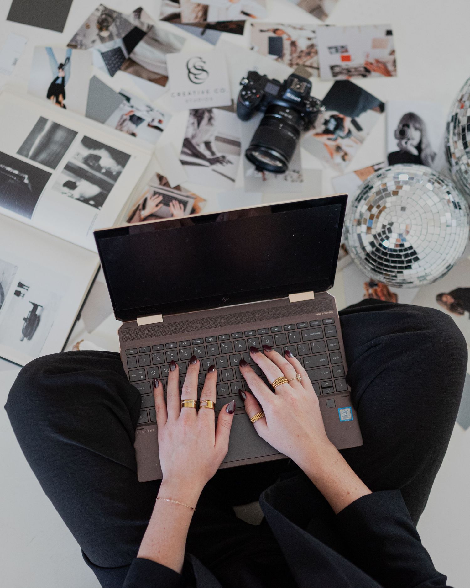 Overhead view of hands typing on laptop surrounded by photos and a disco ball.