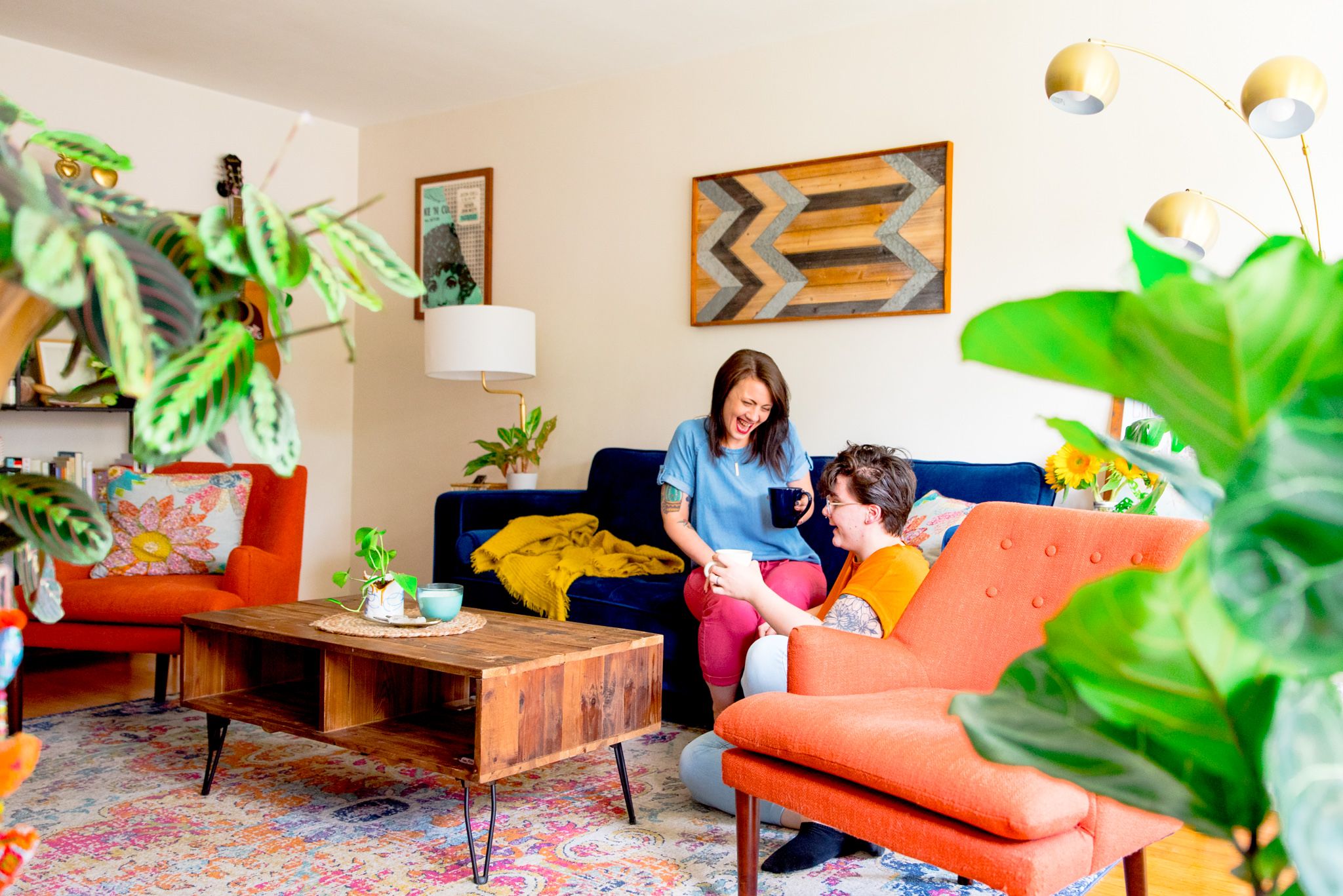 two woman laughing on their blue couch in living room full of plants for Chicago couples pictures