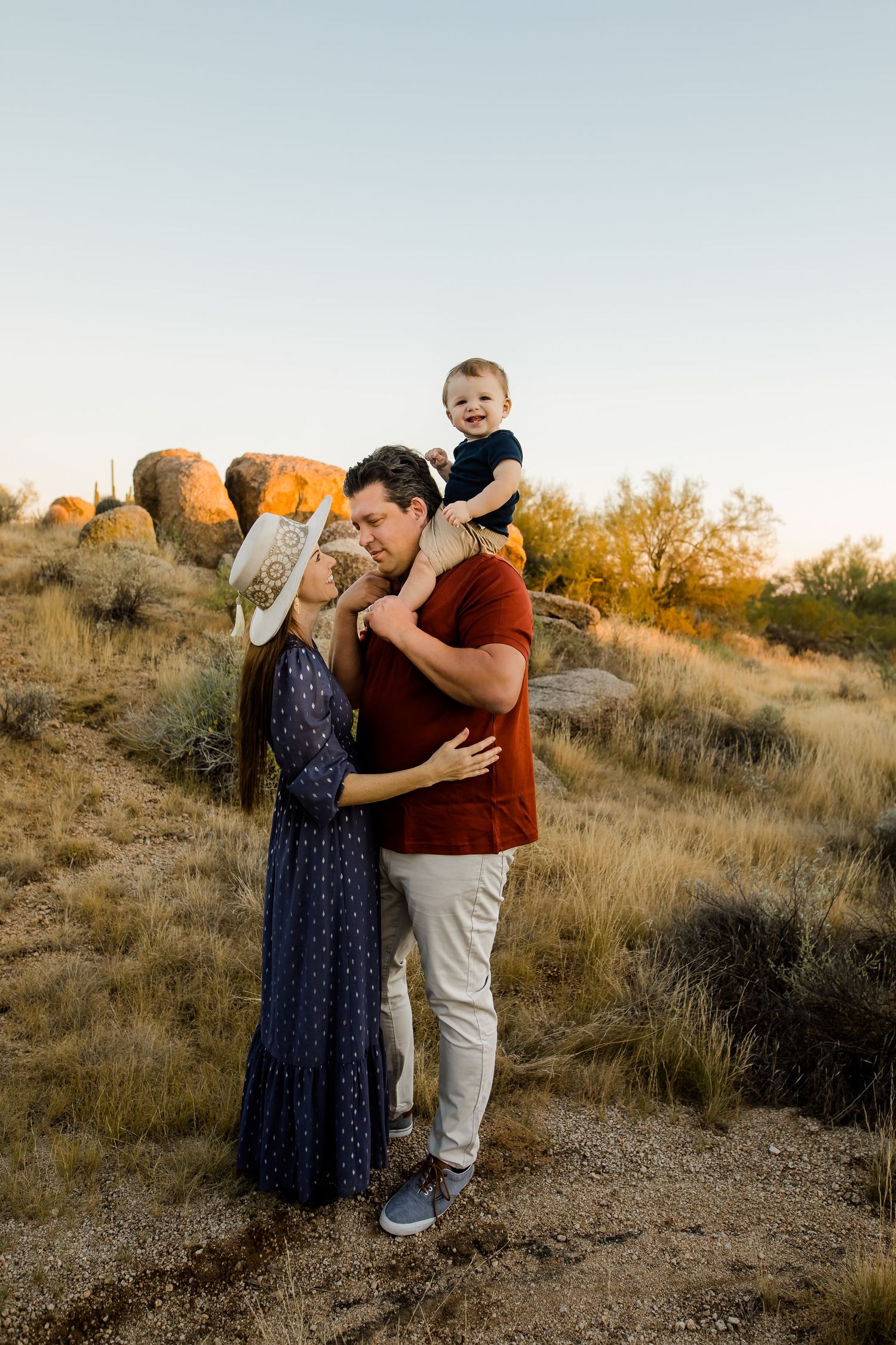 A family stands and loves on each other in front of the beautiful boulders of the Scottsdale Arizona desert at sunset.