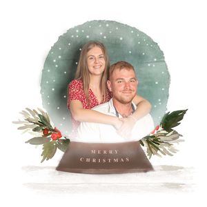 Couple embrace inside a white snow globe with the writing Merry Christmas on the globe stand