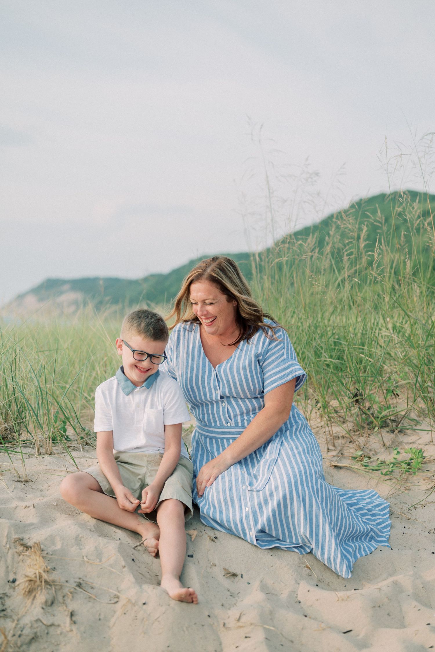 A joyful moment shared on a sandy beach with dunes and tall grass in the background.