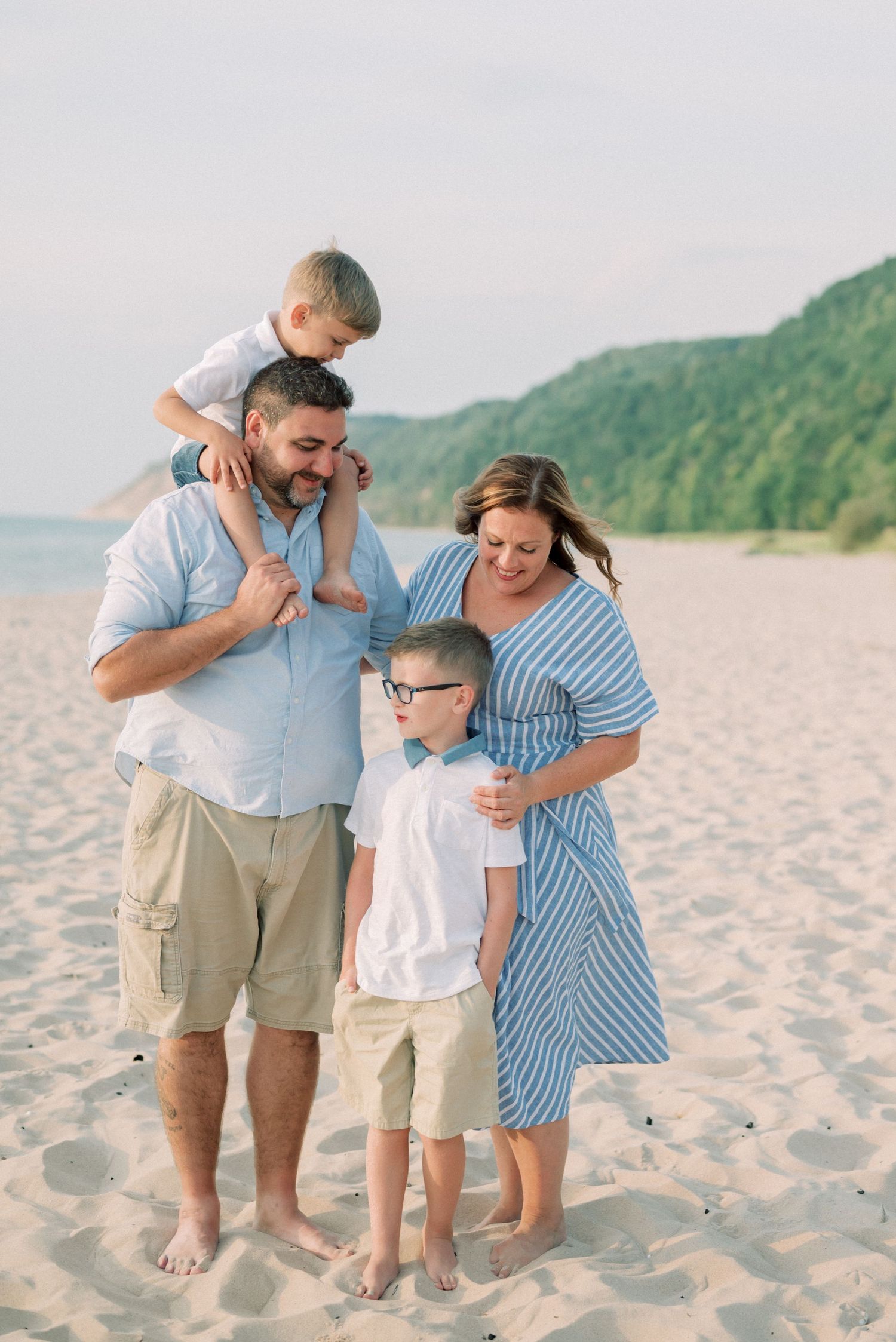 Family enjoying a tender moment together on a scenic beach with green hills in the background.