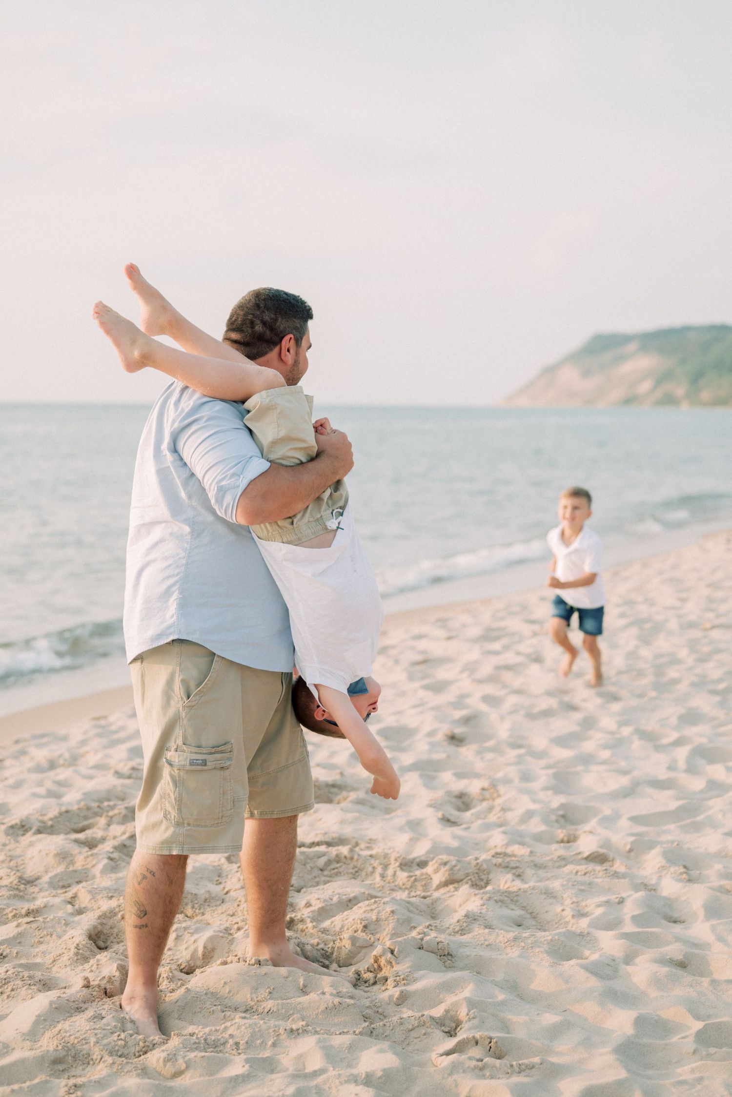 Playful family moment on beach with someone being lifted against coastal backdrop.